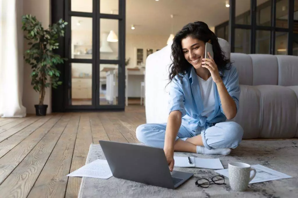 Happy young woman using laptop computer for online video conference, having mobile phone call at